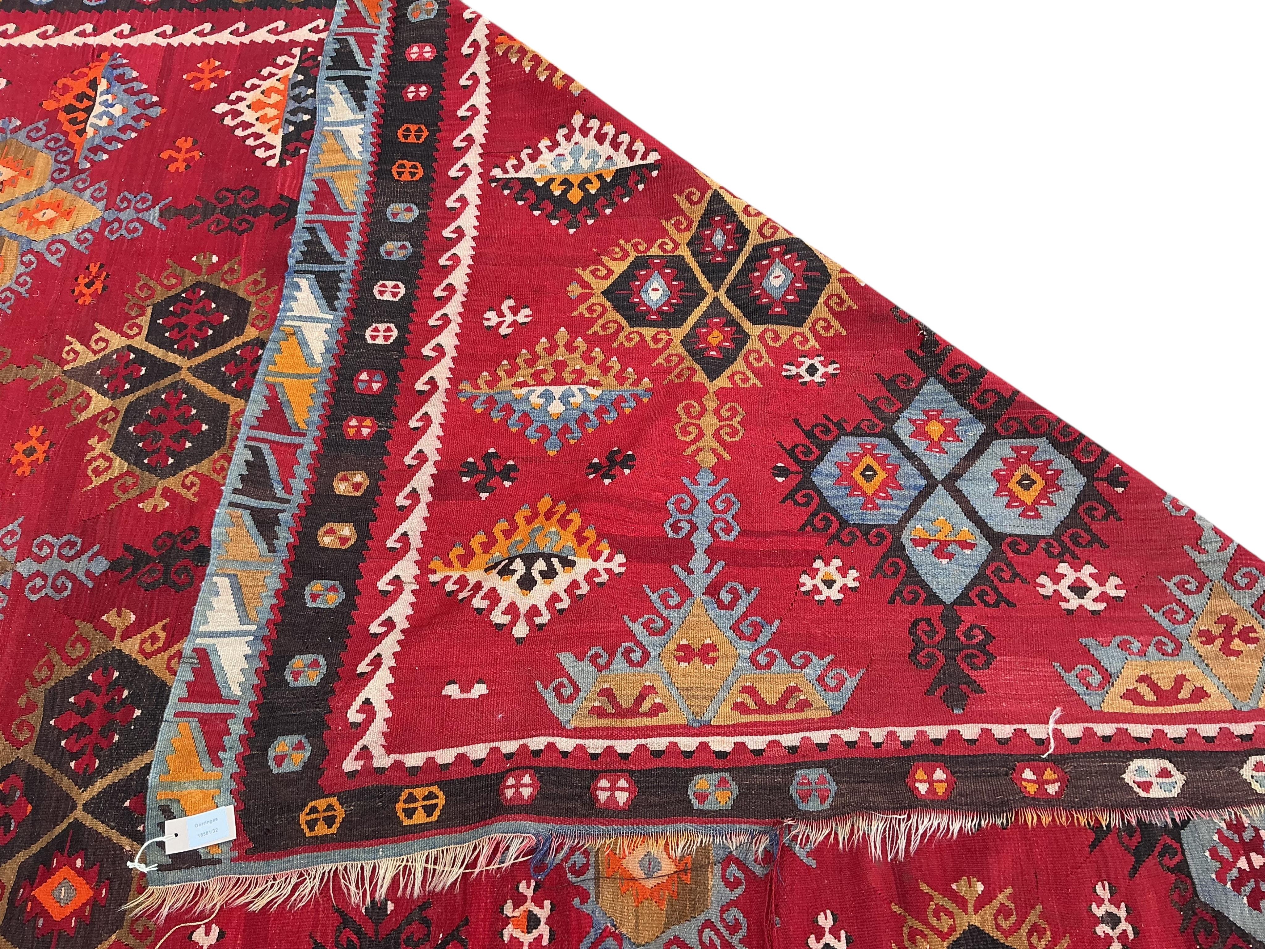A Turkish Anatolian polychrome flatweave Kilim carpet, woven with geometric lozenges on a red field, 367 x 292cm